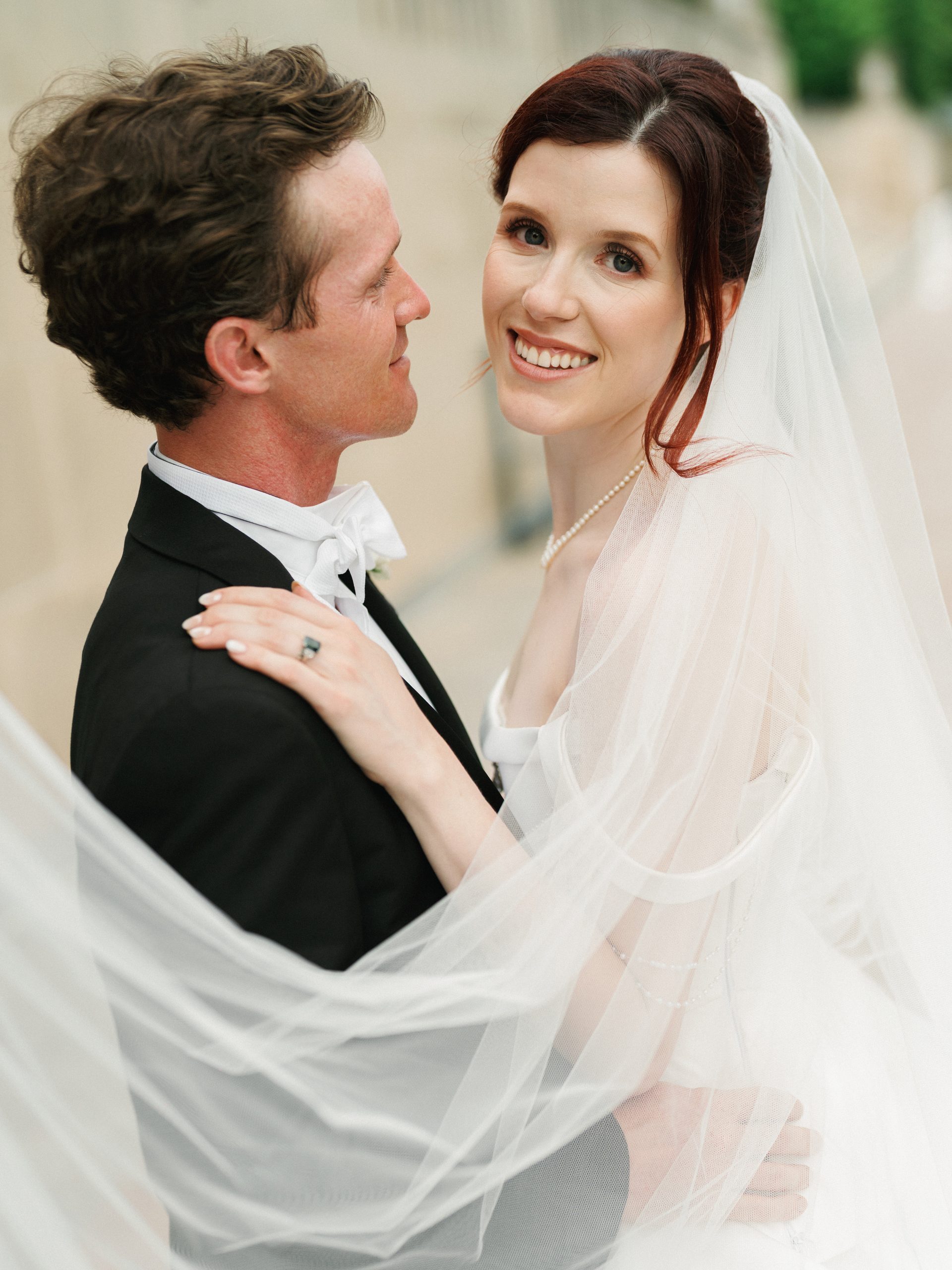 Close-up portrait of a bride smiling through her veil while embracing her groom, showcasing romantic and timeless wedding photography styles.