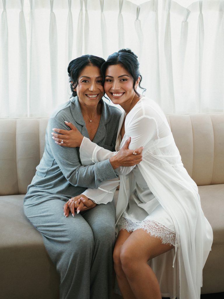 Beautiful bride in a white lace robe hugging her mother during morning prep