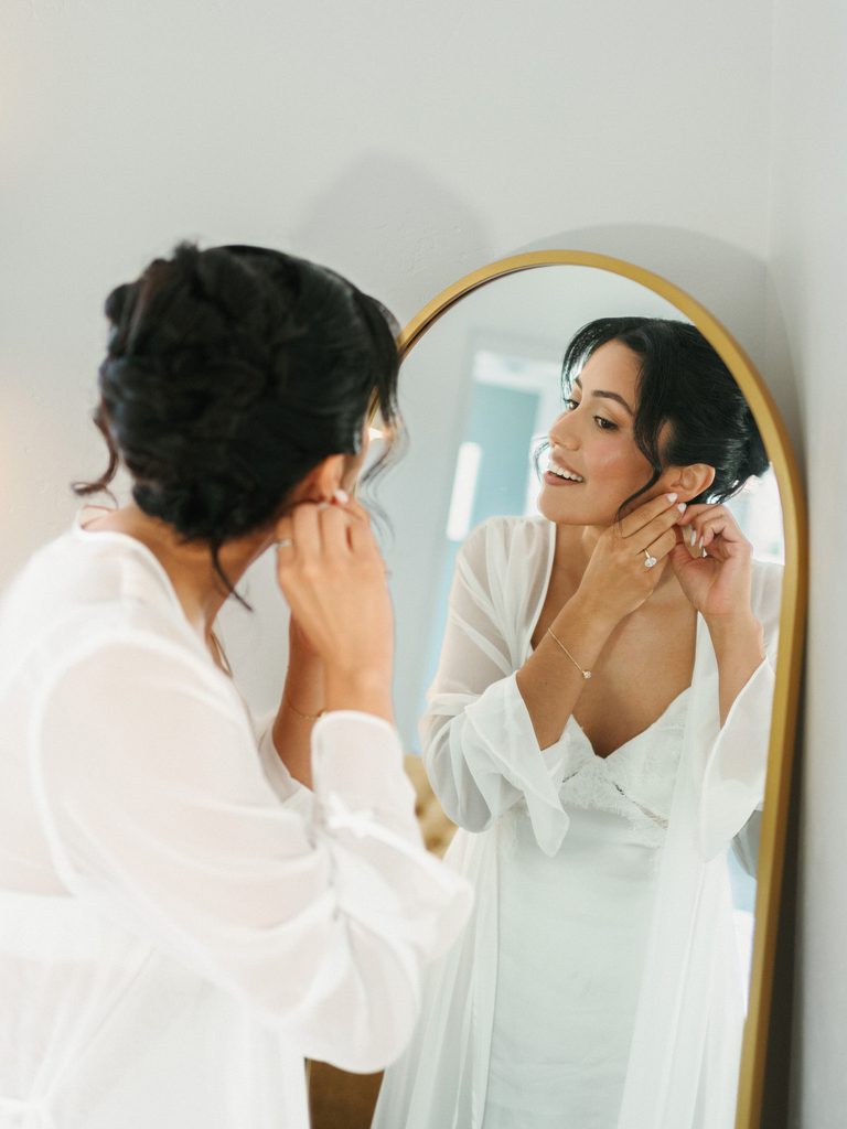 Candid bridal prep moment inside a luxury dressing room with a gold oval mirror