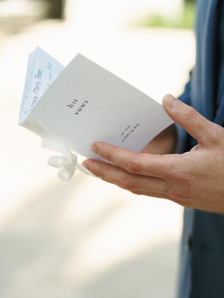 Groom holding an open white his vows card with handwritten romantic text