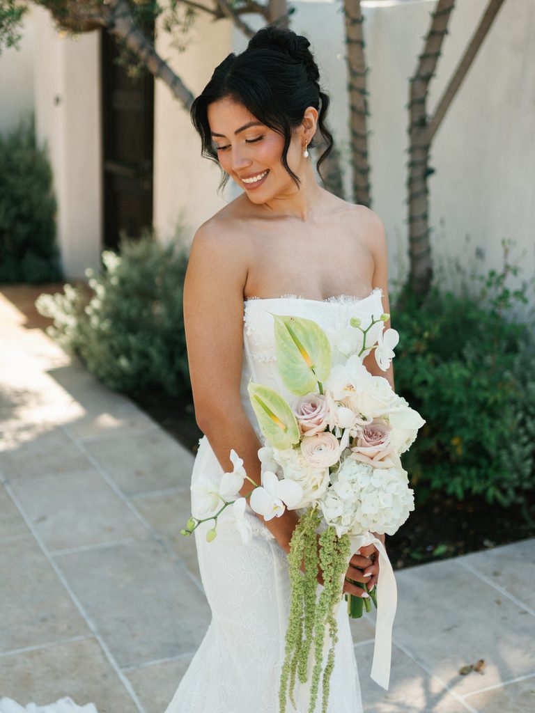 Gorgeous bride looking down at her unique tropical wedding flowers with white orchids