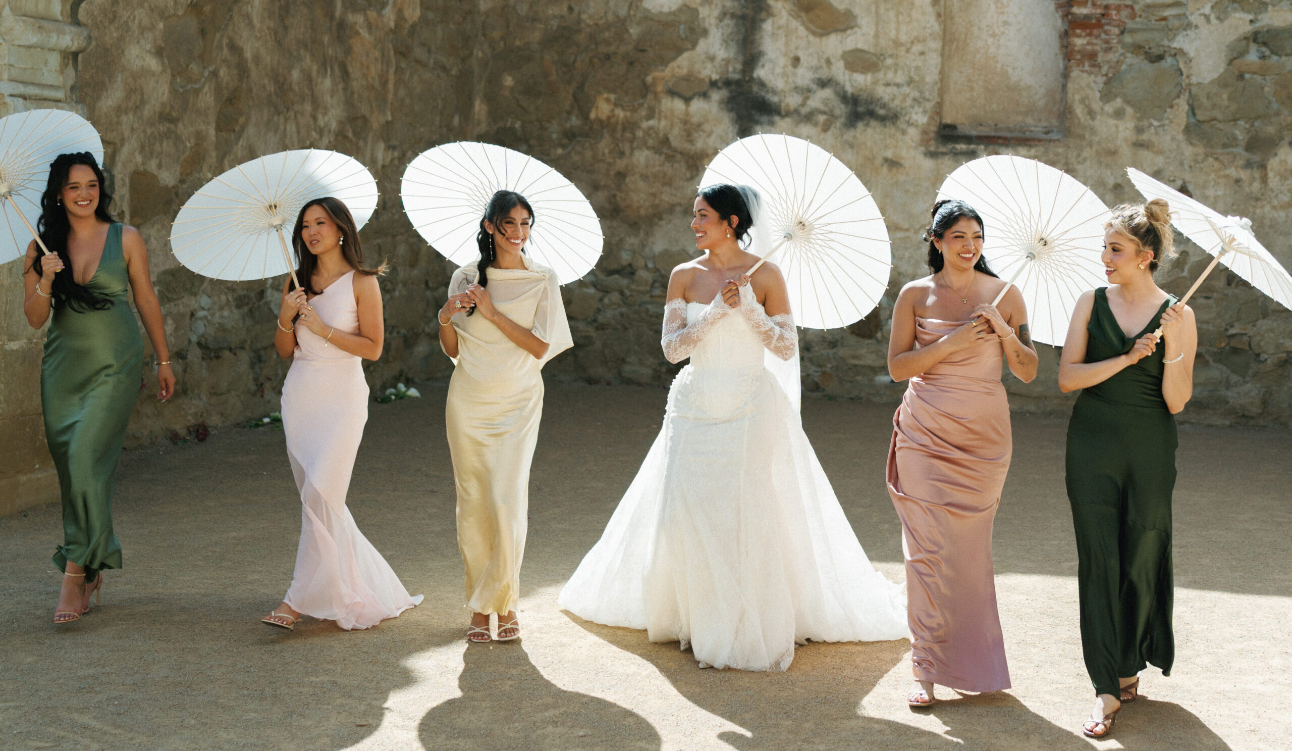 Elegant bridal party group photo featuring colorful silk gowns and classic wooden sun protection umbrellas