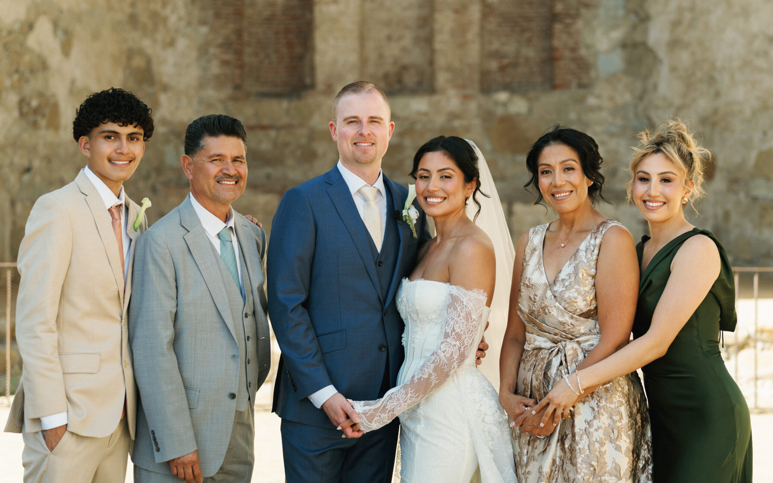 Luxury bride and groom posing with family members against a historic stone wall backdrop