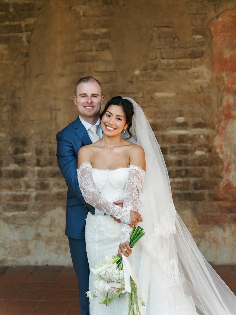 Beautiful bride holding a white rose bouquet while her groom embraces her from behind
