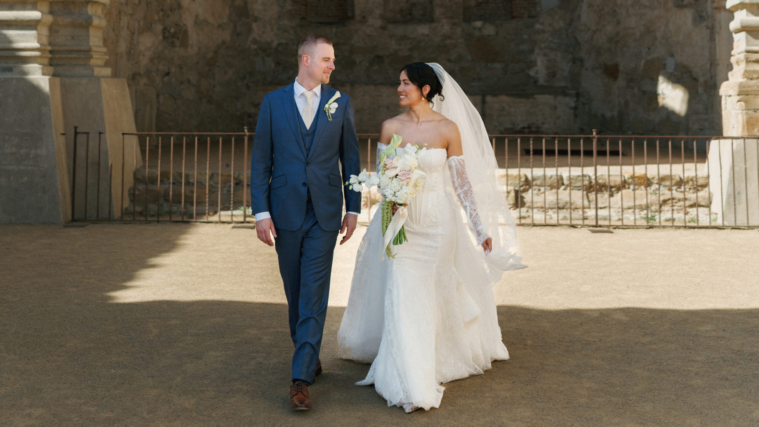 Elegant bride and groom looking at each other while walking outside a historic villa