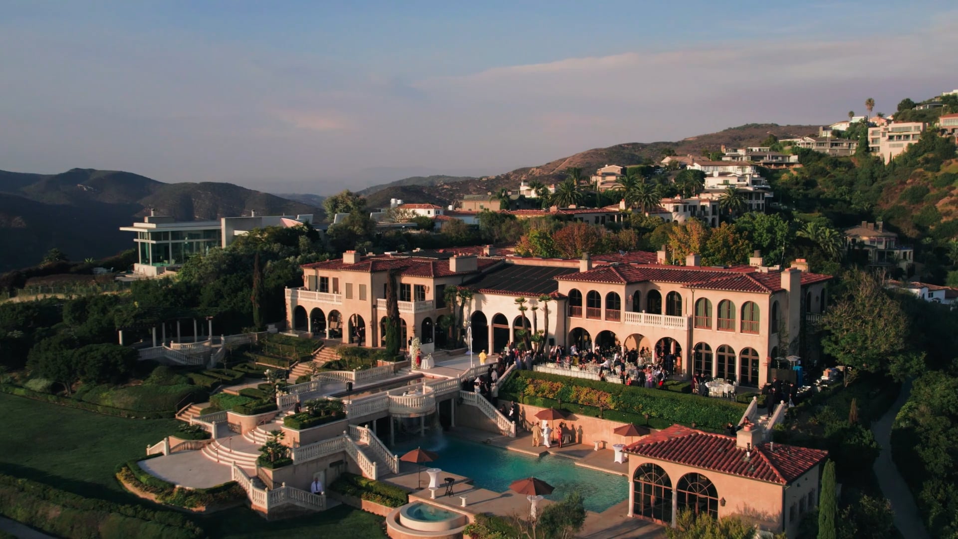 Large hillside building and terraces viewed from above during an outdoor event.