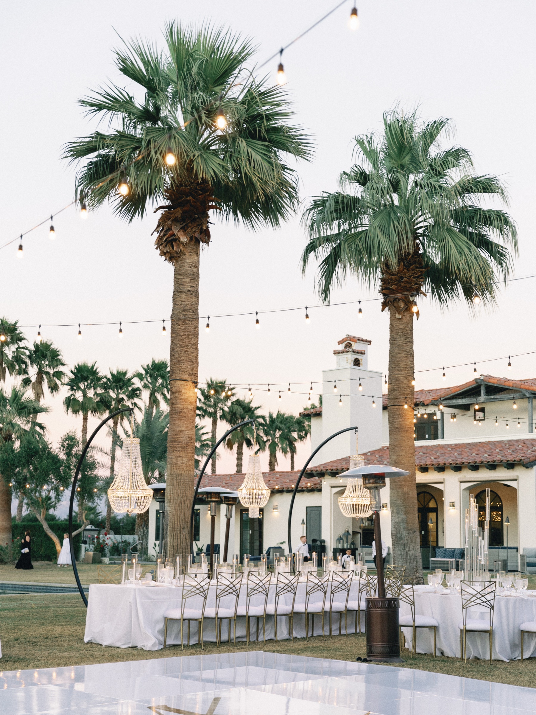 Outdoor wedding reception tables beneath palm trees and string lights