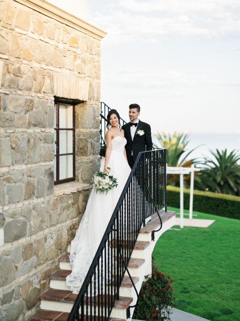 Bride and groom pause on stone steps overlooking the coast