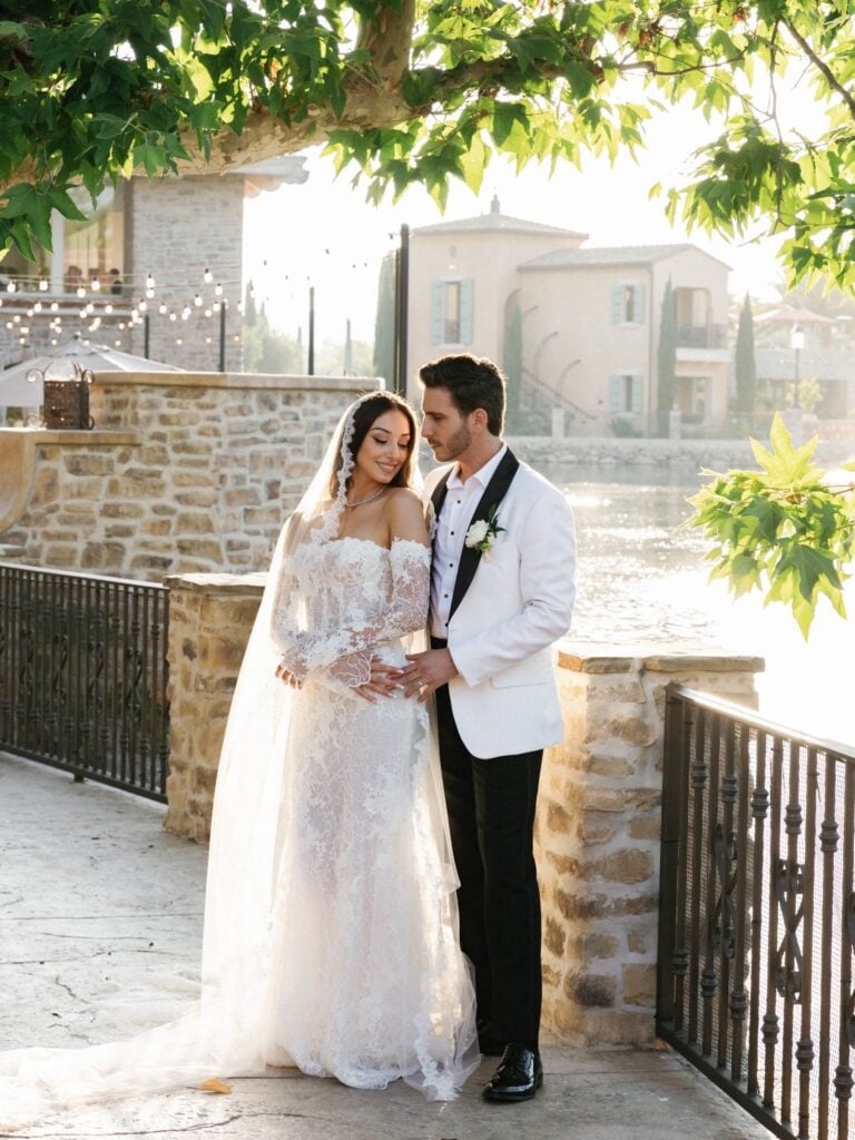Bride and groom stand together beside the water in late-afternoon light