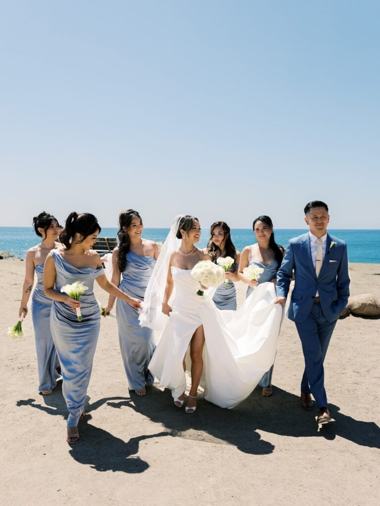 Bride and groom walk with their wedding party beside the water