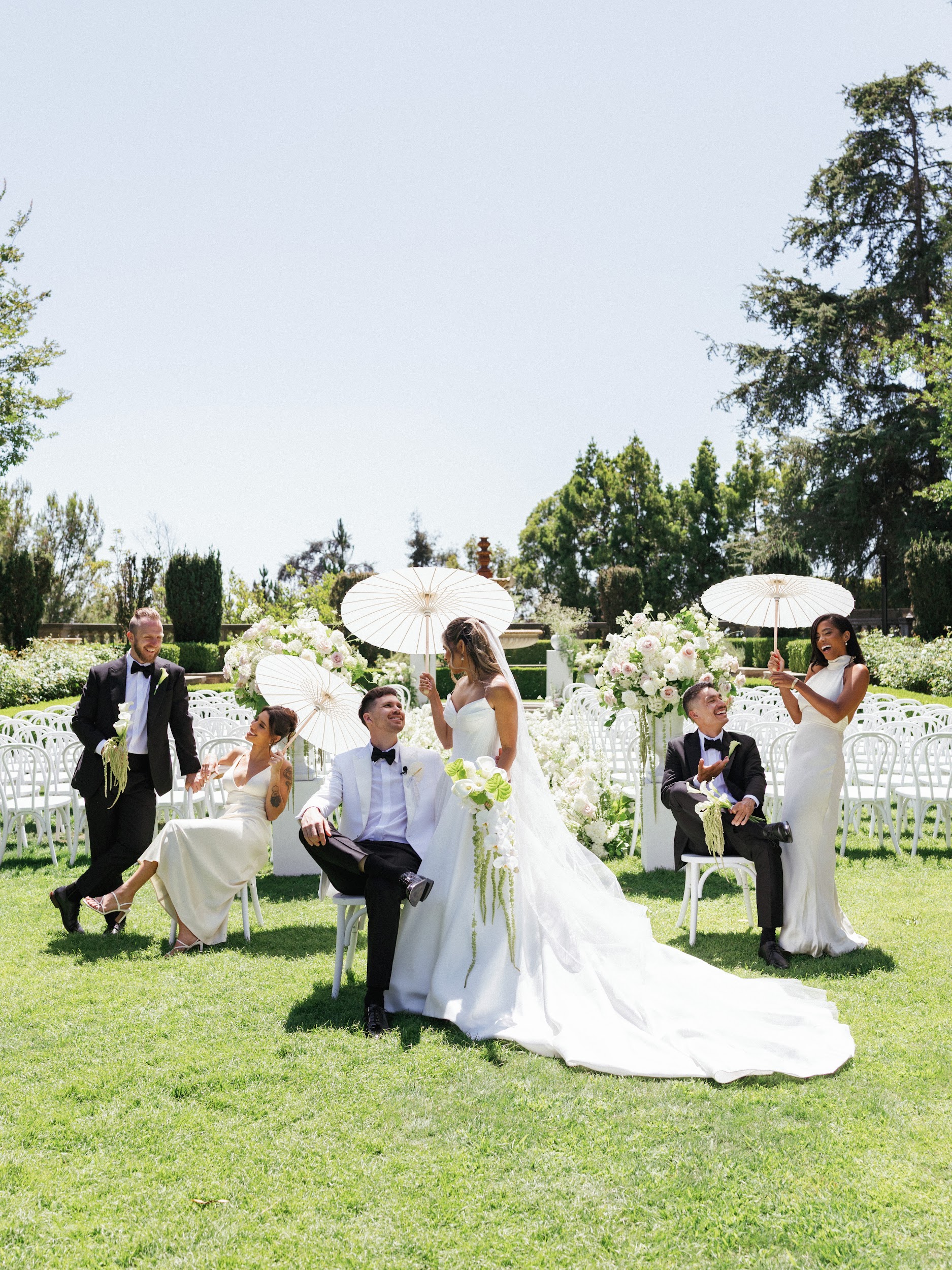 Wedding party among white ceremony chairs and floral arrangements on a lawn.