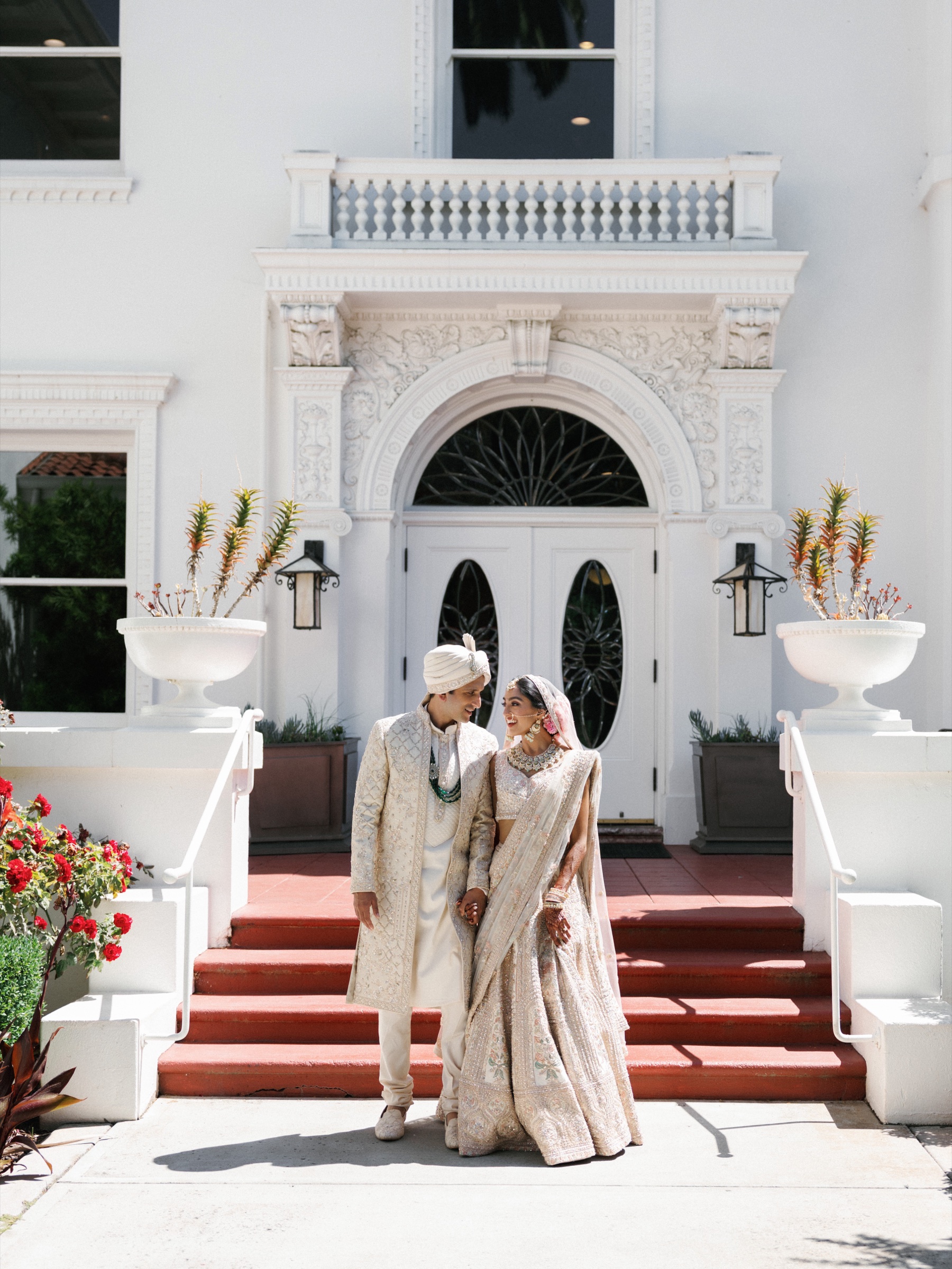 Newlyweds stand on red steps outside an ornate white stucco building