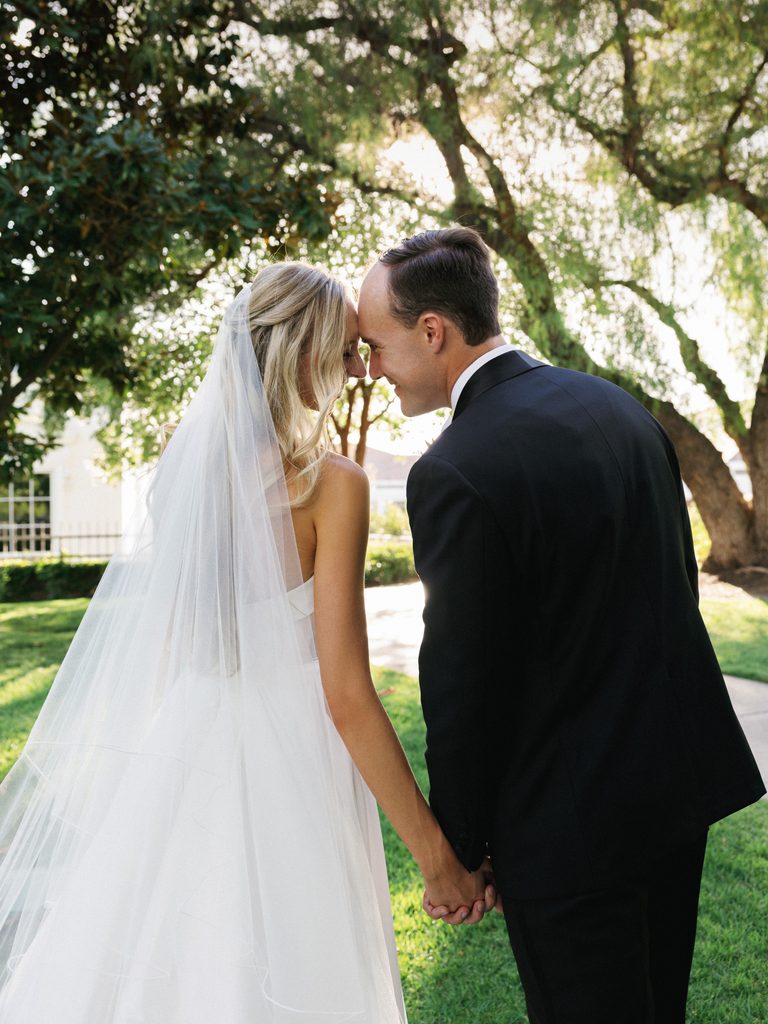 Intimate newlyweds portrait from behind holding hands and smiling at each other showcasing a delicate sheer wedding veil