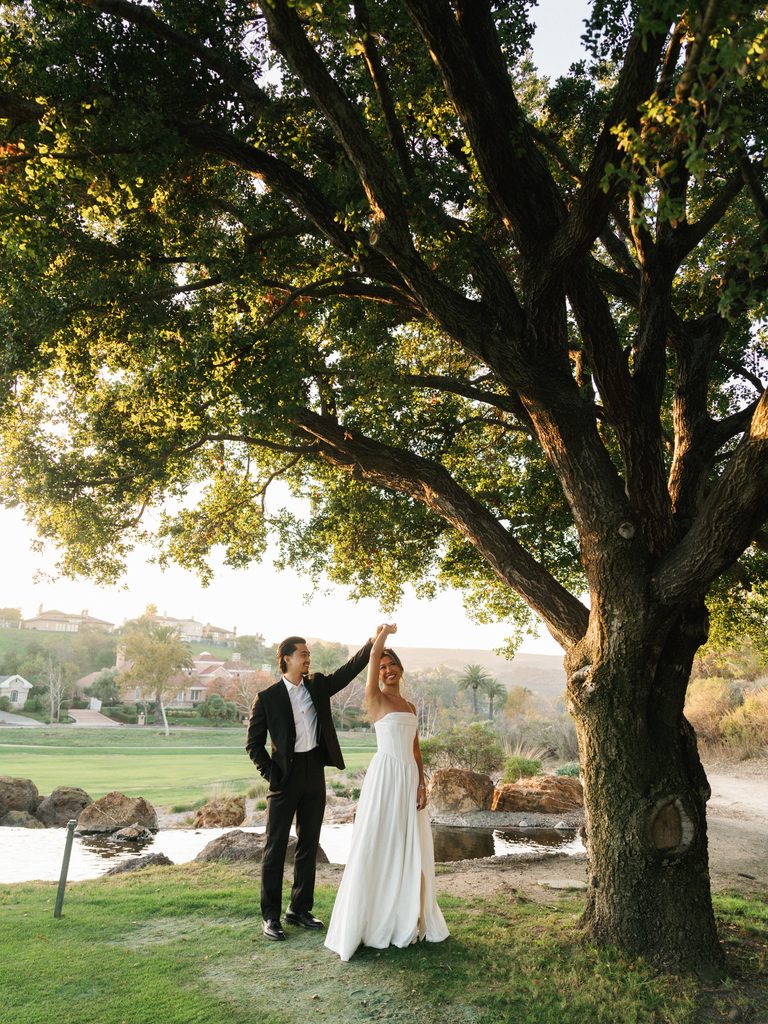 Elegant groom spinning his laughing bride in a strapless satin gown during a romantic outdoor wedding dance session at sunset