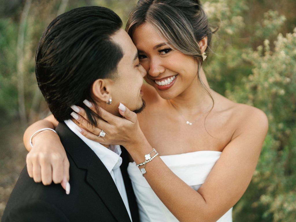 Intimate close up wedding portrait of a joyful bride embracing her groom showing her diamond engagement ring and luxury silver clover charm bracelets