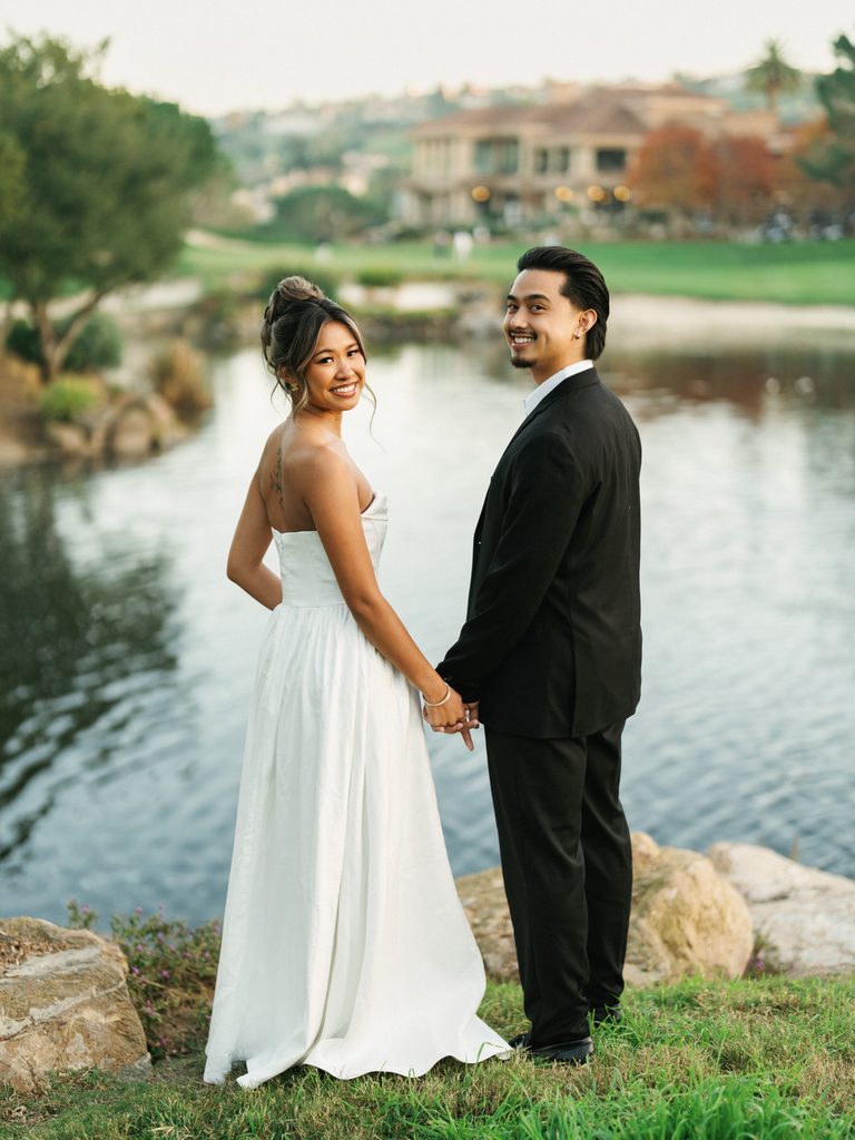 Gorgeous bride looking back over her shoulder smiling and holding hands with her groom outside an upscale country club estate