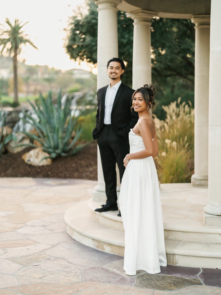 Sophisticated future bride and groom posing near stone pavilion steps showcasing a tropical resort garden landscape background view