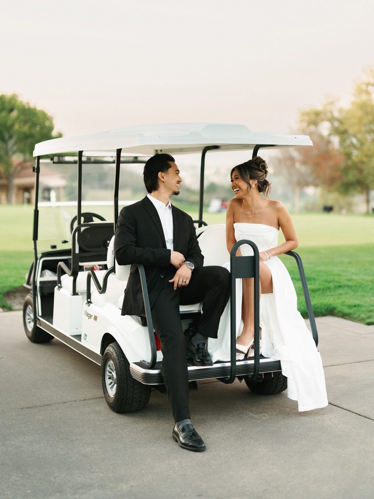 Laughing newlyweds sitting and talking in a white golf cart during a luxury country club country estate wedding photo session