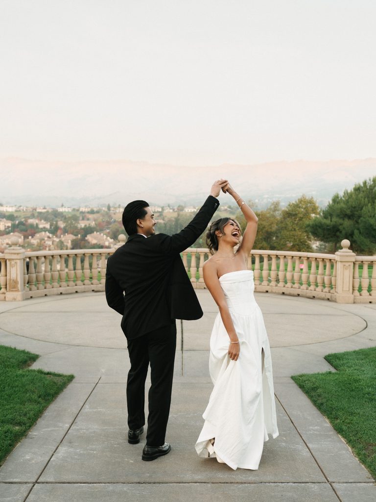Joyful newlyweds dancing and twirling on a scenic stone overlook balcony during their luxury destination wedding photo session