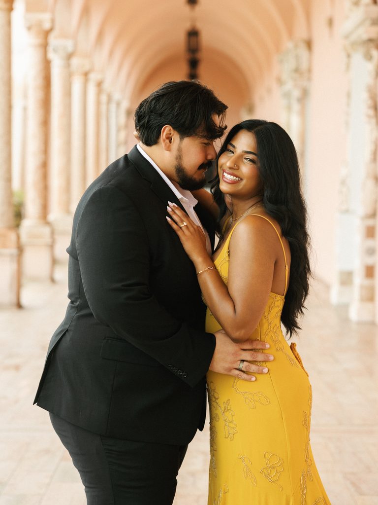 Couple posing under a classic loggia, inspiring vibrant and elegant engagement photo outfits.