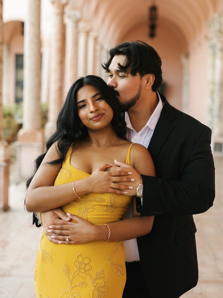 Groom-to-be in a black blazer kissing a bride-to-be in a yellow slip dress, showing bold color choices for engagement photo outfits.