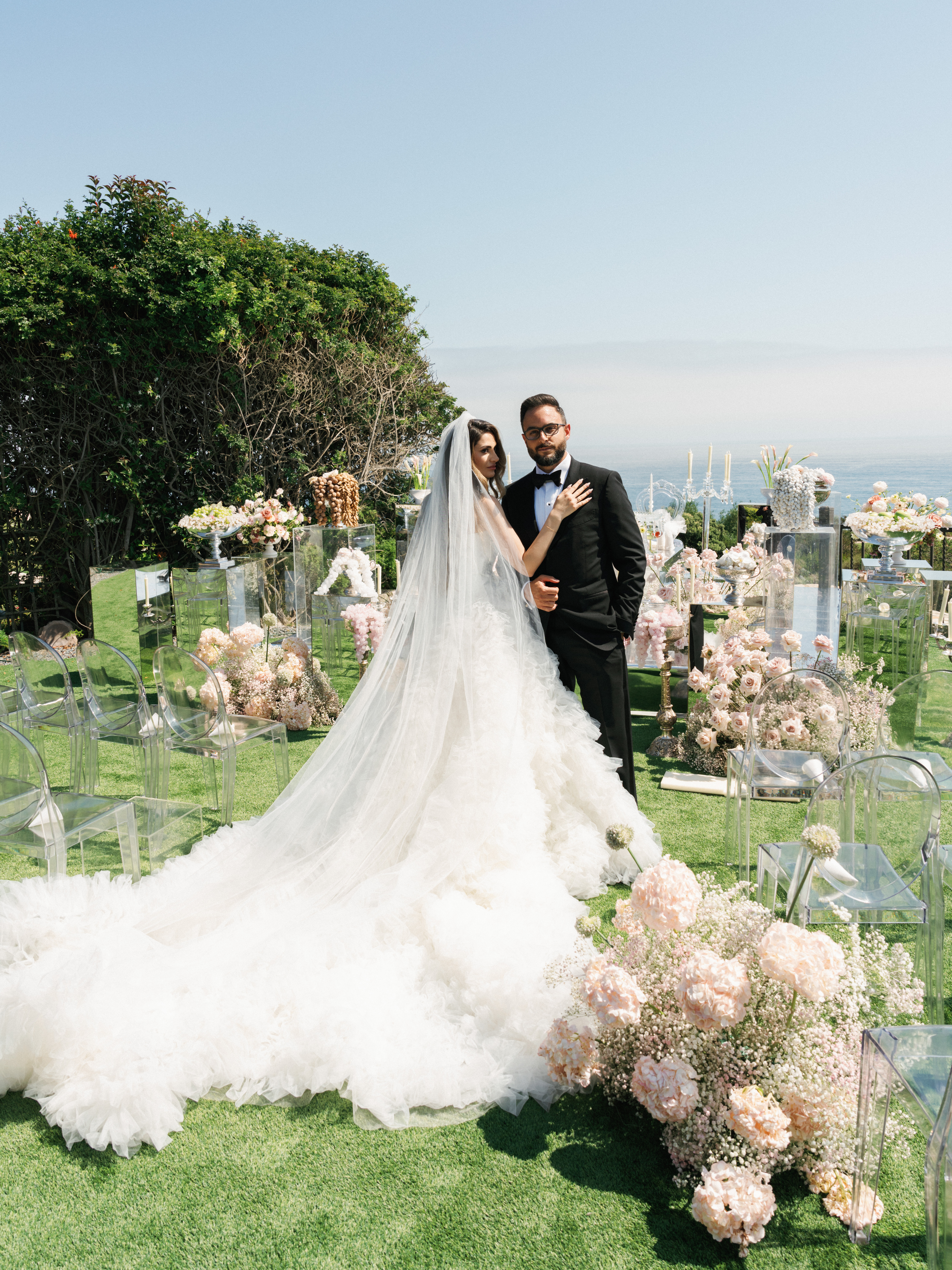 Bride and groom pose together showcasing a stunning long train wedding dress and veil at a luxury outdoor ceremony venue