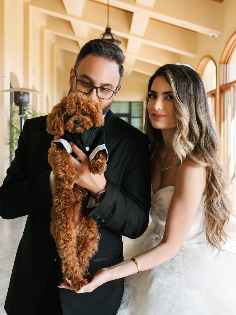 Newlyweds pose with their adorable pet poodle during an elegant indoor portrait session