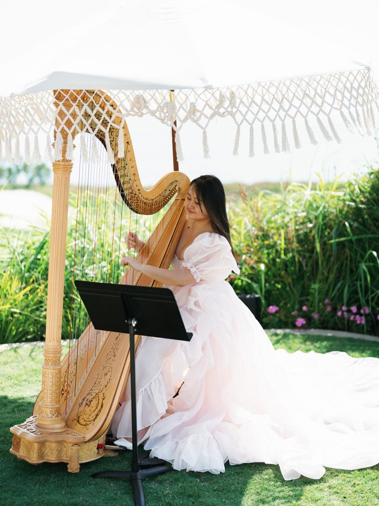 Professional harpist plays a golden harp under a macrame umbrella at a luxury coastal wedding