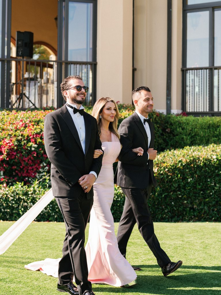 Wedding party members walk down the grassy aisle together during a beautiful upscale processional captured in these wedding ceremony photos
