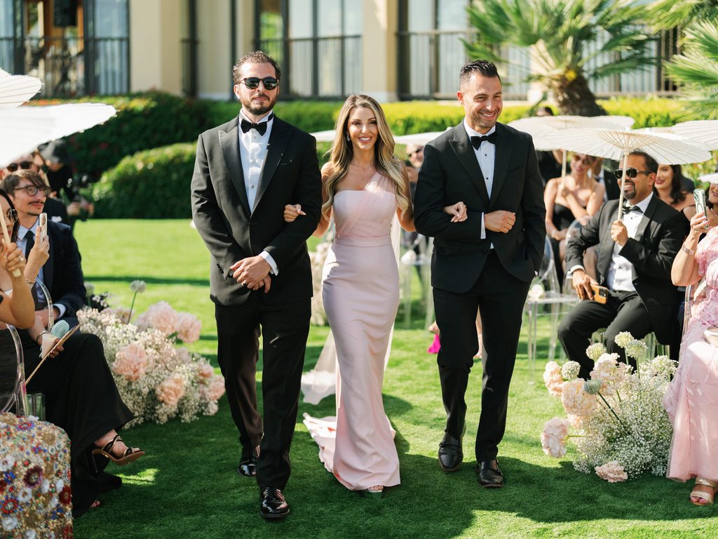 Bridesmaid in a blush pink dress walks with two groomsmen during a luxury outdoor celebration highlighting elegant wedding ceremony photos