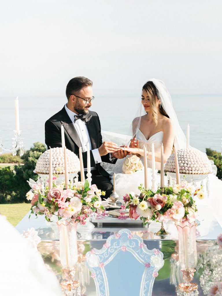 Groom places a ring on the brides finger during a traditional Persian wedding ceremony overlooking the ocean