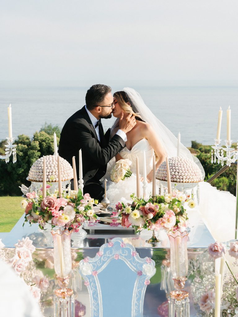 Romantic bride and groom share a beautiful kiss behind a mirrored floral table in these luxury wedding ceremony photos