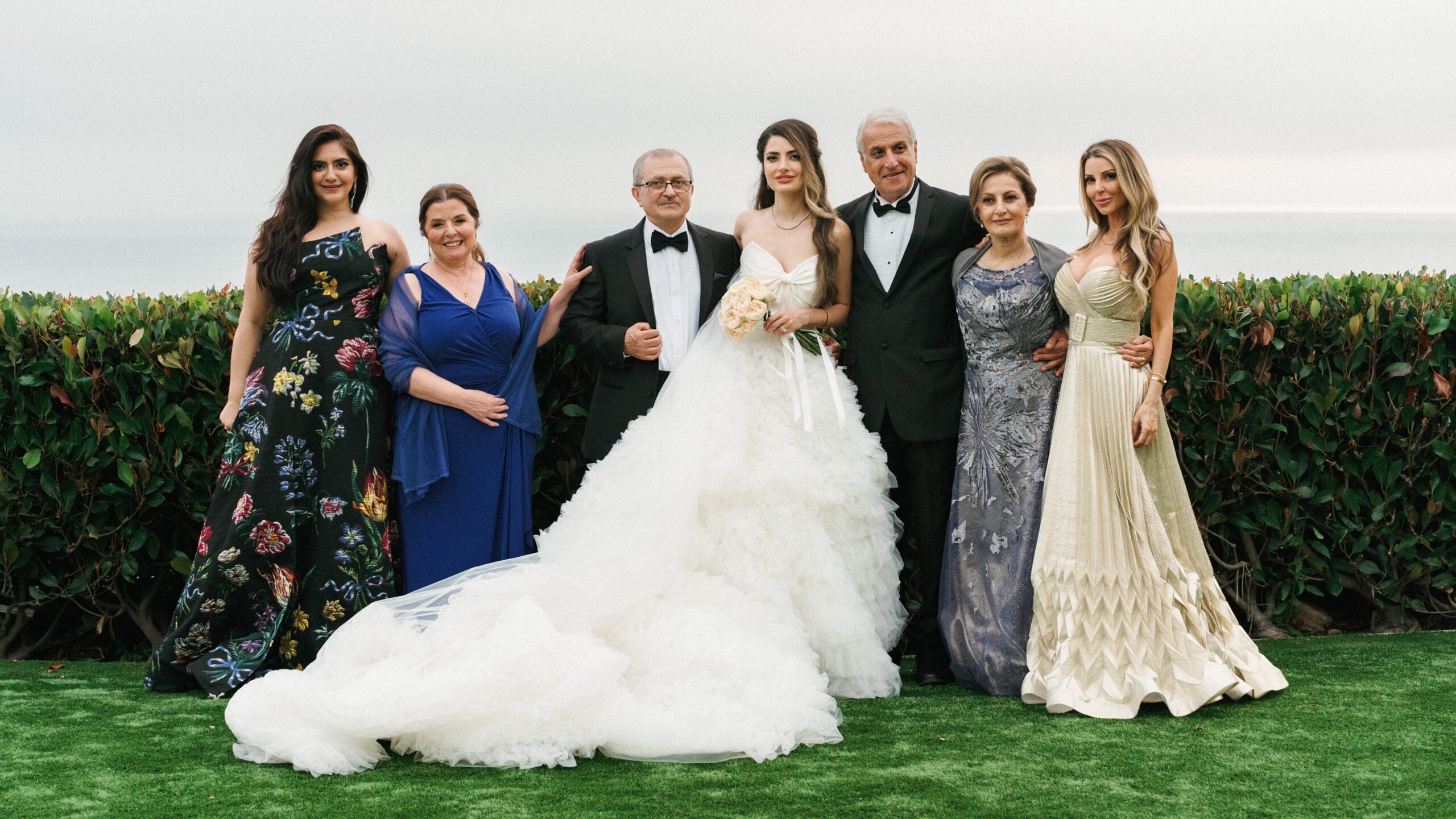 Elegant bride poses for family formal portraits with her parents and relatives during a luxury outdoor coastal wedding