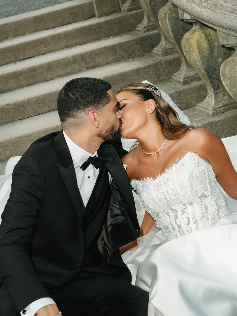 Romantic newlyweds sharing a passionate kiss while sitting outdoor on historical garden stairs during an upscale estate photo session
