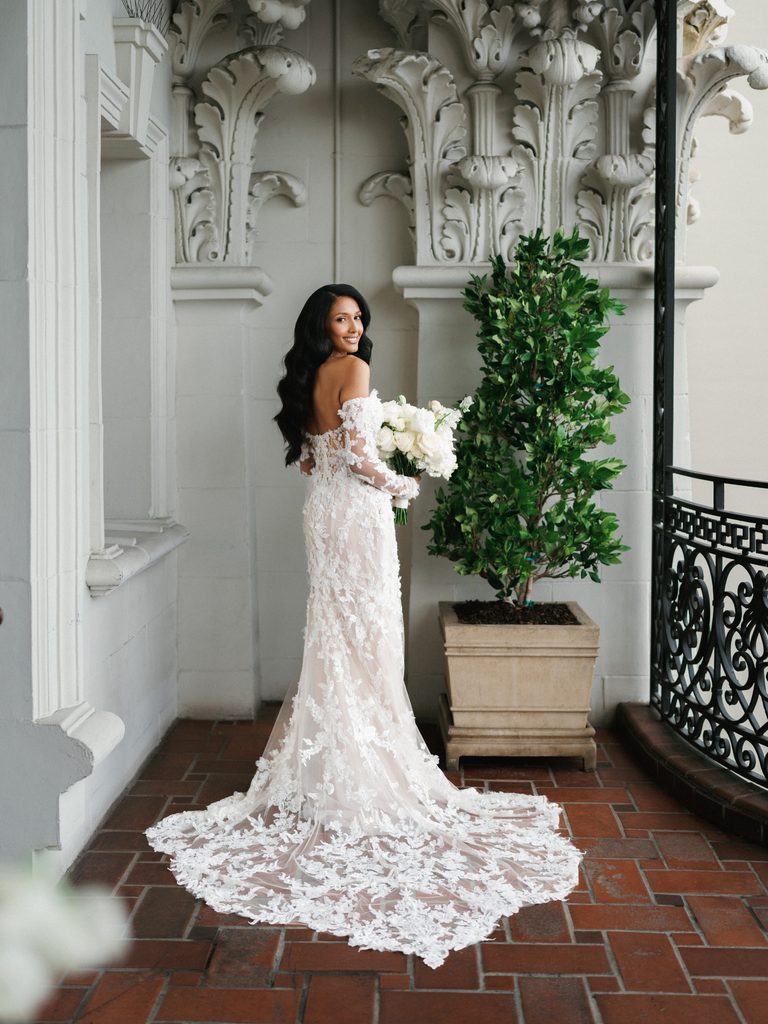 Elegant bride looking back on a luxury hotel terrace displaying her long lace train wedding dress highlighting why professional lighting details trump raw wedding photos