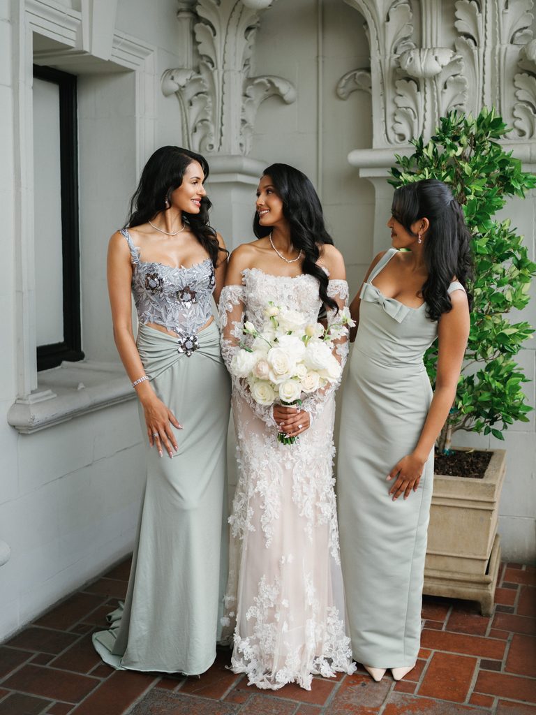 Beautiful bride smiling with bridesmaids wearing elegant sage green dresses with corset and bow details on a luxury hotel terrace