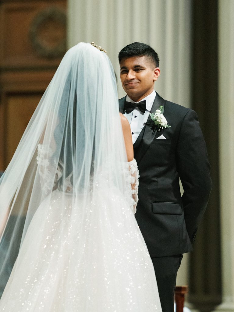 Emotional groom looking at his beautiful bride under a cathedral veil during an intimate luxury church ceremony altar moment