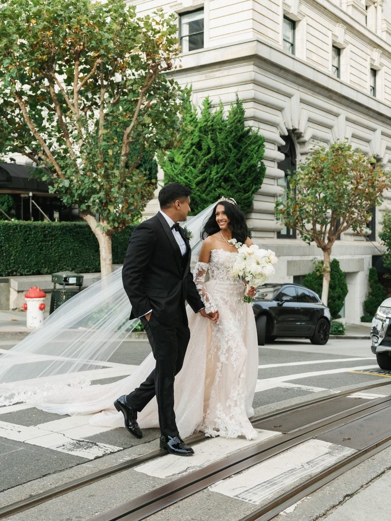 Cinematic city wedding couple walking hand in hand across a street with historical cable car tracks in front of grand architecture
