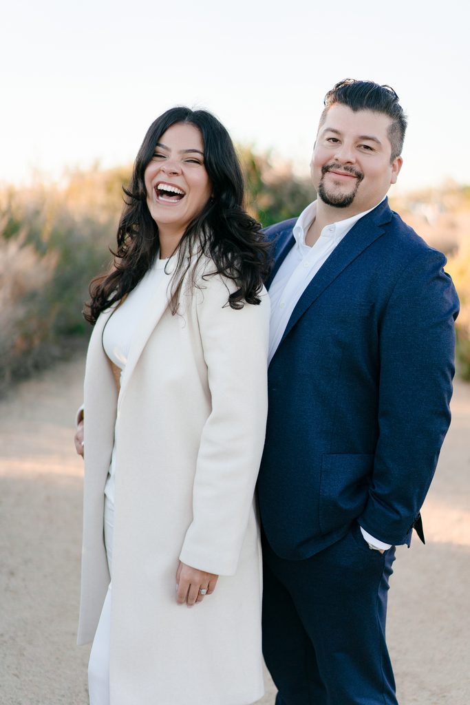 Couple in a navy blazer and white winter coat laughing together, inspiring classy cold-weather engagement photo outfits.