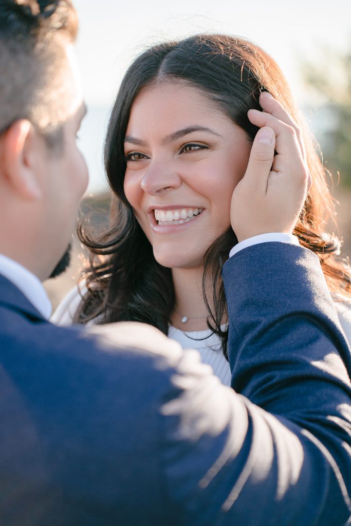 Man in a navy suit touching a smiling woman's hair, showcasing romantic styling for engagement photo outfits.