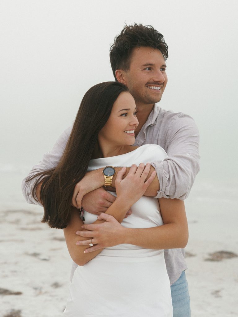 Couple smiling and looking away from the camera during a foggy overcast coastal photoshoot.