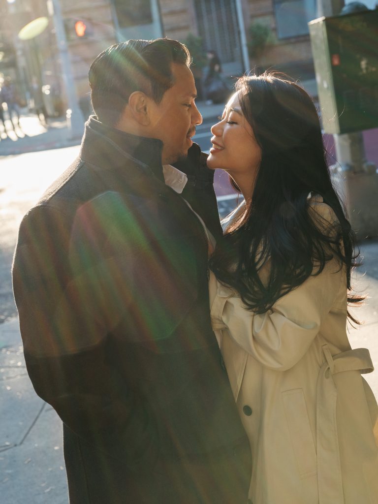 Newlyweds-to-be sharing an intimate look on a city street corner under bright afternoon sunlight.