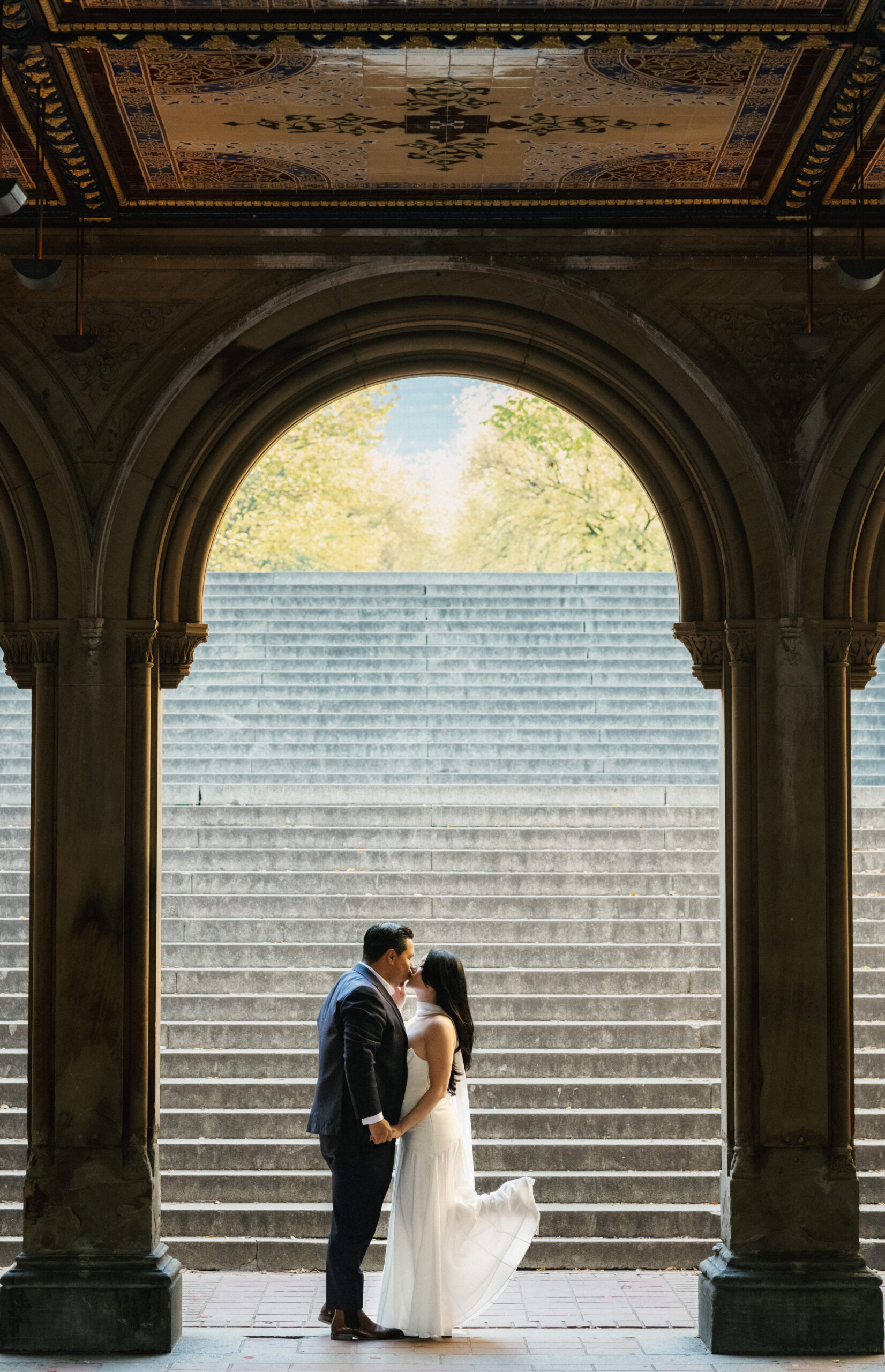 Cinematic kiss under a grand stone archway framing creative Central Park engagement photo ideas