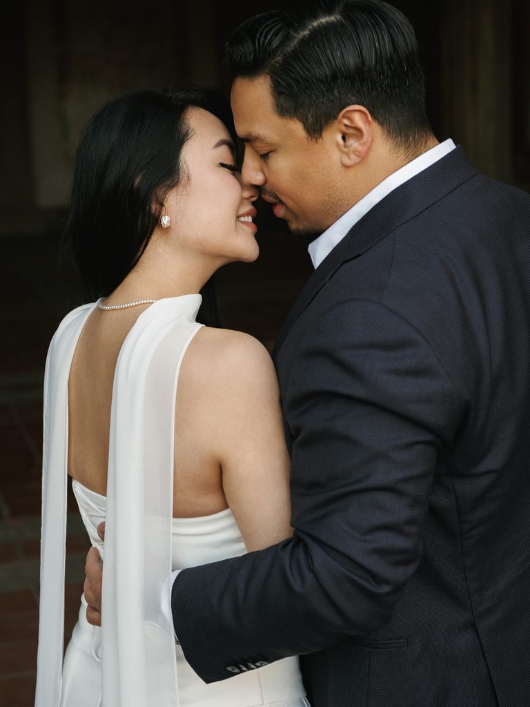 Groom to be leaning in close to his smiling fiance wearing a white halter top with a long silk scarf