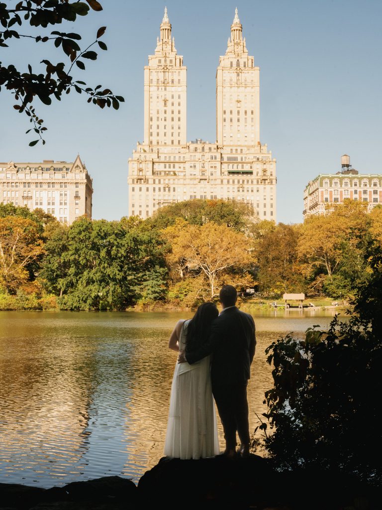 Back view of a couple standing by the lake facing the San Remo towers for classic NYC engagement photo ideas