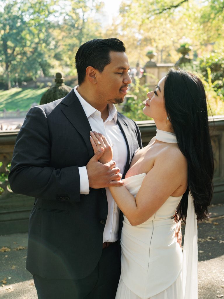 Elegant couple posing by Bethesda Terrace stone railing for high end Central Park engagement photo ideas