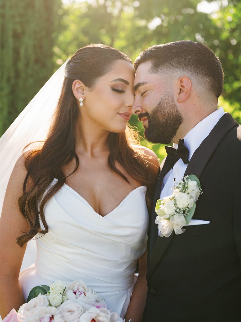 Romantic close up bridal portrait of a groom leaning into his gorgeous bride with her eyes closed in beautiful warm garden backlight