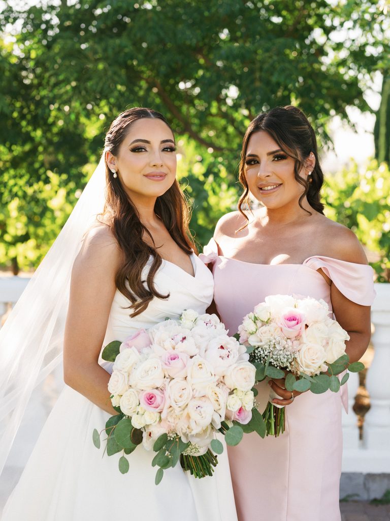 Sophisticated bridal portrait of a beautiful bride and her maid of honor wearing a stylish off the shoulder pastel pink gown with elegant wedding makeup