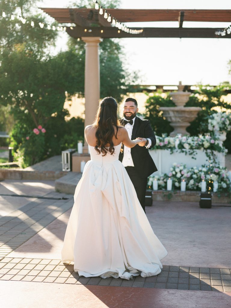 Joyful groom spinning his gorgeous bride showing the dramatic back detail of her strapless white ballgown dress during a scenic outdoor reception dance