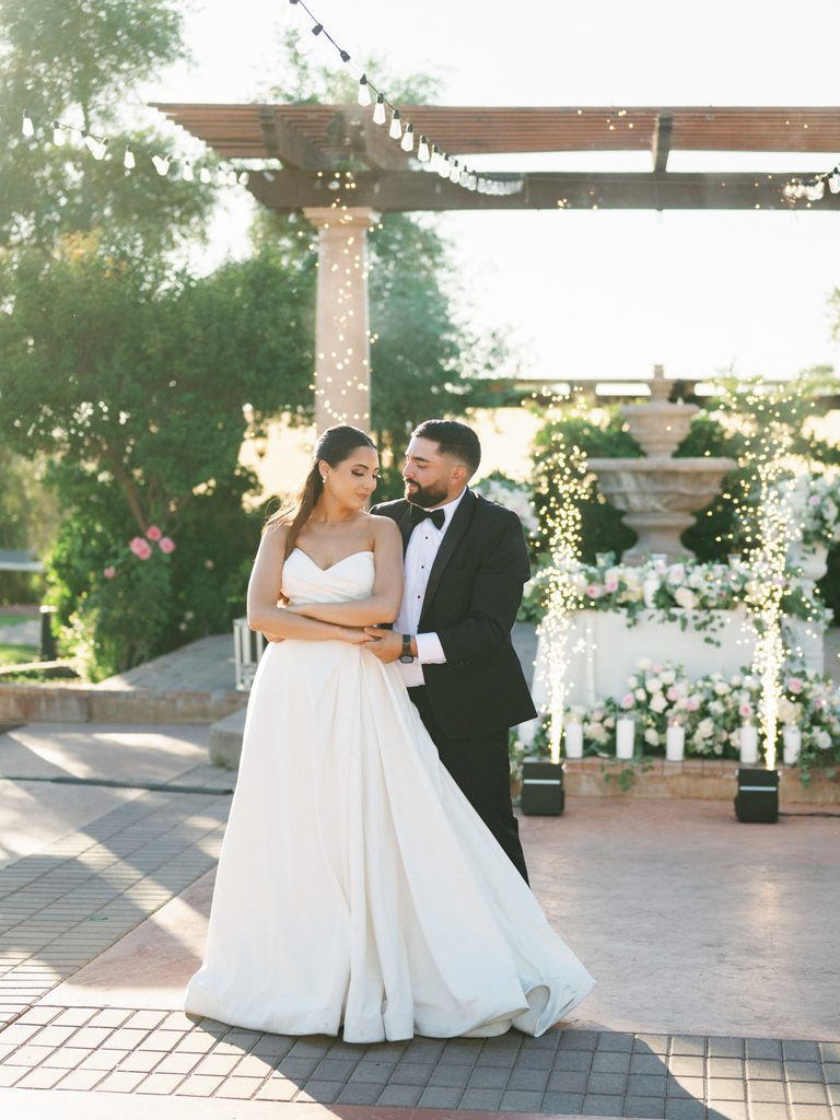 Breathtaking first dance portrait of a luxury couple posing next to outdoor cold sparklers fountains with an elegant stone altar and hanging string lights